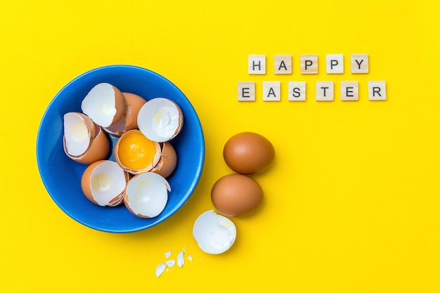 Bright creative postcard with happy easter text raw eggs yolk and shell in a blue plate on a yellow .