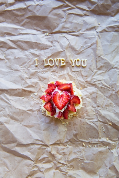 Bright cupcake with strawberries lies on craft paper, the inscription I love you