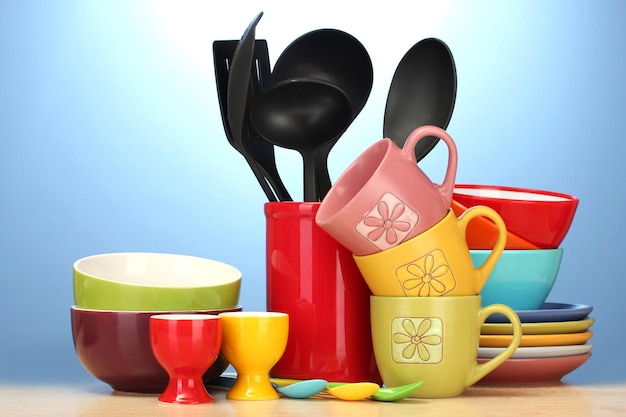 Photo bright empty bowls cups and kitchen utensils on wooden table on blue background