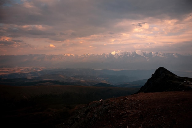 素晴らしい夕日と薄明と明るい霞を背景に岩が多い丘のある明るい夜の審美的な山の風景。谷の自然の美しさ。