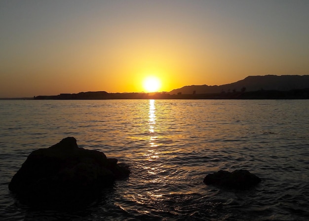 地平線上の明るい夕日が穏やかな海面を照らします