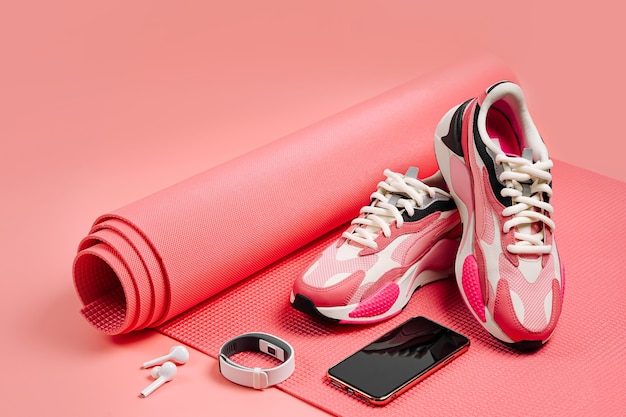 Bright fashion sneakers with smartphone, fitness bracelet and pink yoga mat. App for training indoors. Online Fitness program. Home online workout.