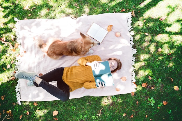 bright fun autumn girl and dog Corgi lie on a plaid on the lawn and read books