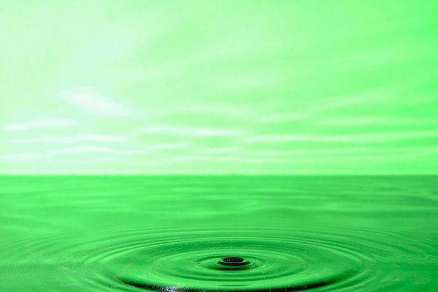 地表水に落下した水滴から円が発散する明るい緑色の背景。