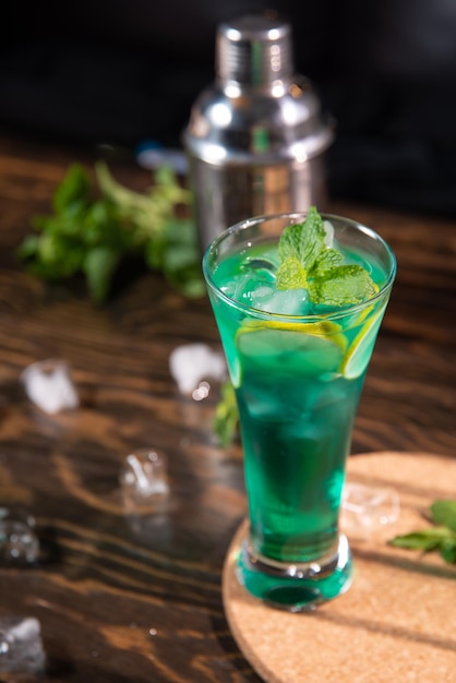 a bright green cocktail with lemon and mint in a large transparent glass