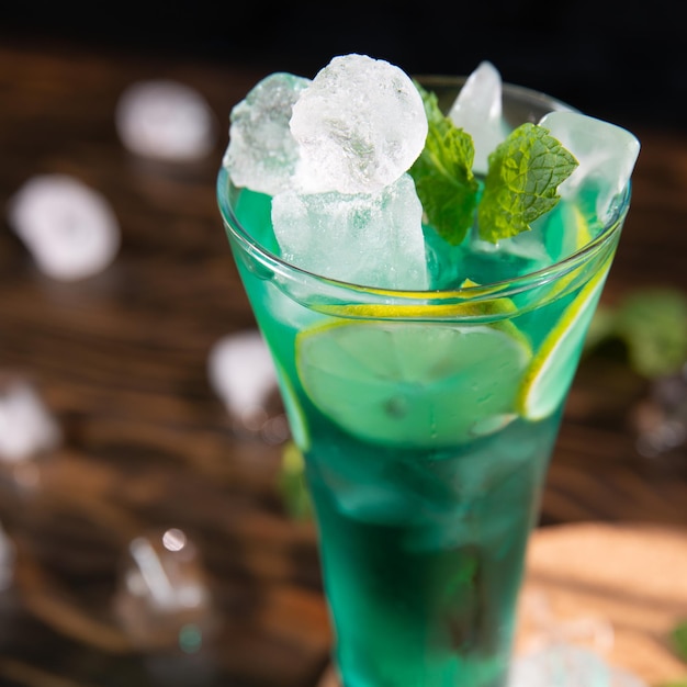 a bright green cocktail with lemon and mint in a large transparent glass