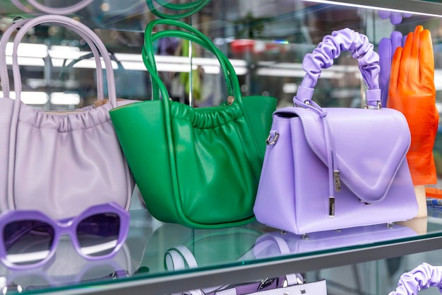 Borse da donna verde brillante e viola e guanti in pelle arancione in una vetrina di vetro accessori moda e stile primo piano