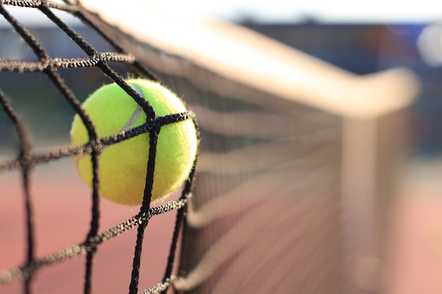 Bright greenish yellow tennis ball hitting the net.