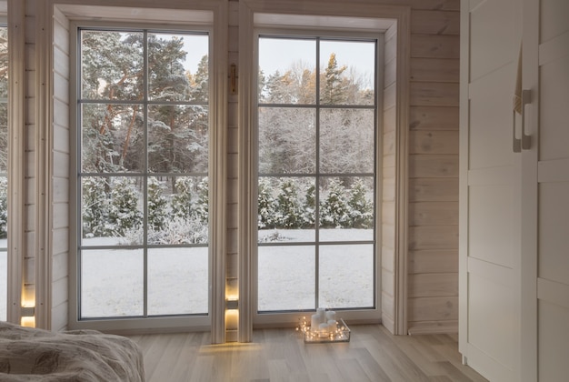 Bright interior of the room in wooden house with a large window overlooking the winter courtyard. Snowy winter landscape in white window. Home and garden, Christmas concept.