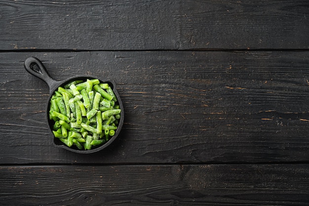 Bright juicy frozen green beans set, in frying cast iron pan, on black wooden table