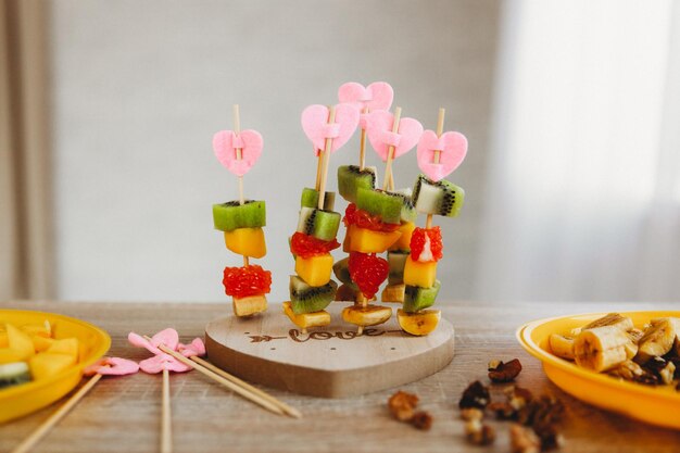 Crostino luminoso di kiwi, mango, banana e pompelmo su un supporto a forma di cuore. gli spiedini di legno sono splendidamente decorati con stupende deliziose tartine