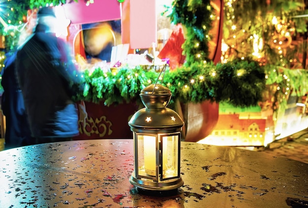 Bright lantern with the candle inside of it standing on one of the tables at the Christmas Market in Riga, Latvia. It is the symbol of cosiness and warmth during the celebrations.