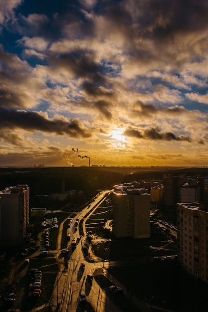 道路や屋根に明るい光がきらめきます。街の素晴らしい夕日の光と影。太陽光線の背景にある煙突からの煙。