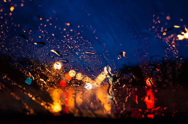 The bright lights of the night city through the glass in the drops of rain. 