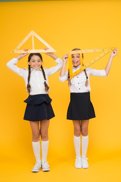 明るい心。黄色の壁で制服を着た子供たち。友情と姉妹関係。幸せな小さな女の子は数学を勉強します。生徒はゴン定規を使用します。幹分野。学校に戻る。数学と幾何学。