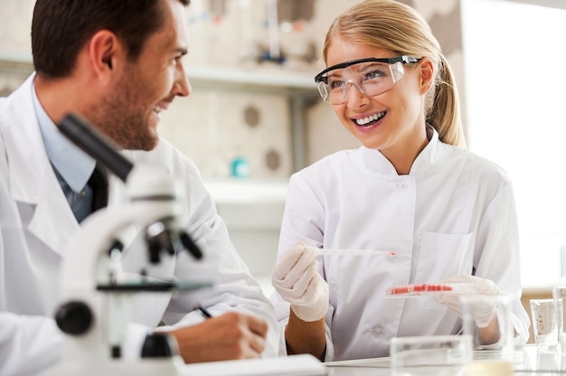 Bright minds at work. Two cheerful young scientists making experiments and looking at each other while sitting in the laboratory