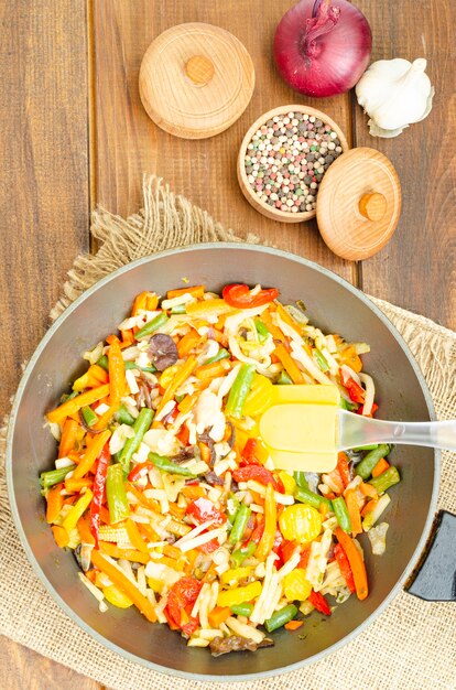 Bright mix of stewed vegetables in frying pan on wooden