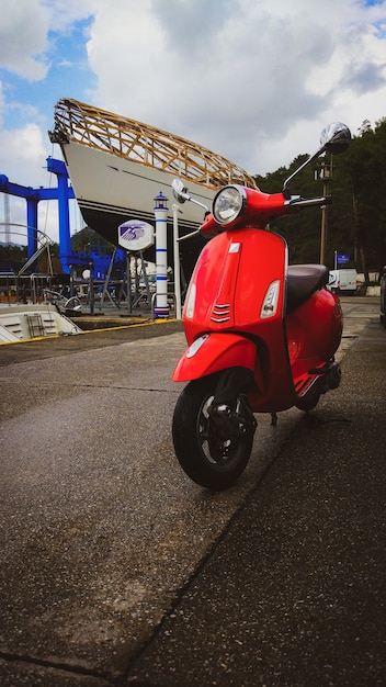 A bright moped stands in the parking lot at the marina with yachts