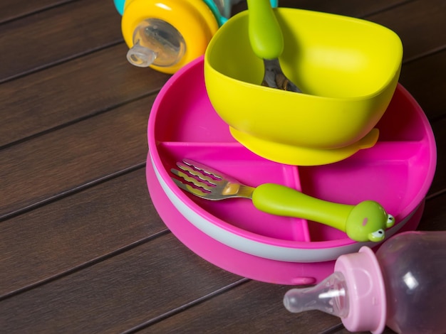 Bright multi-colored children's tableware. spoon fork bowls and sippy cups on wooden table