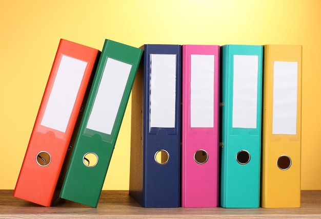 Bright office folders on wooden table on yellow background