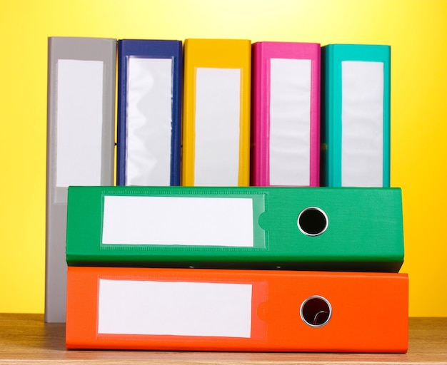 Bright office folders on wooden table on yellow background