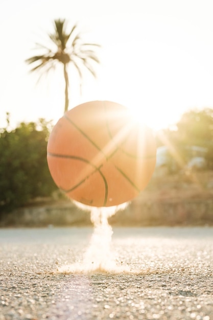 Bright orange ball bouncing on asphalt ground against green trees on sunny day in summer