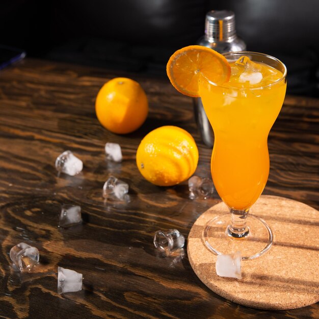 a bright orange cocktail with orange slices and ice in a large transparent glass top view