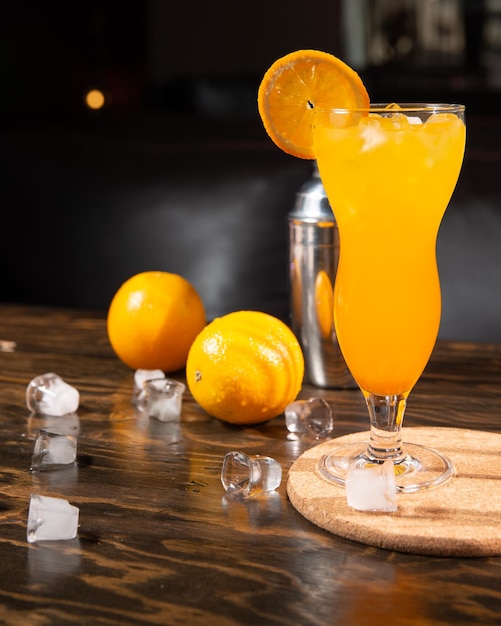 a bright orange cocktail with orange slices and ice in a large transparent glass