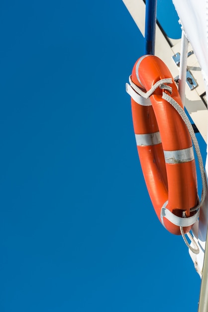 Bright orange lifebuoy on a white yacht side. Blue sky background