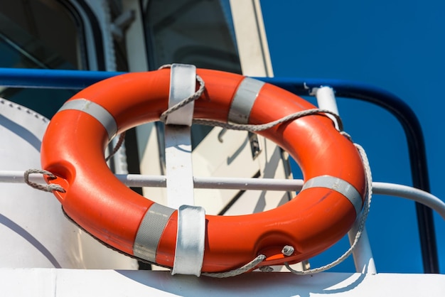 Ярко-оранжевый спасательный круг на белой стороне яхты. Фон голубого неба