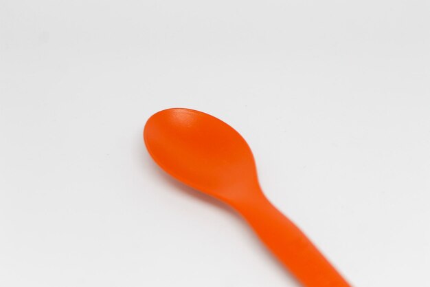 A bright orange spoon with a red handle sits on a white surface.