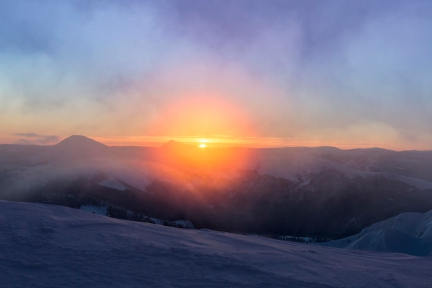 Bright orange sunrise of the sun disk in the snowy\
mountains