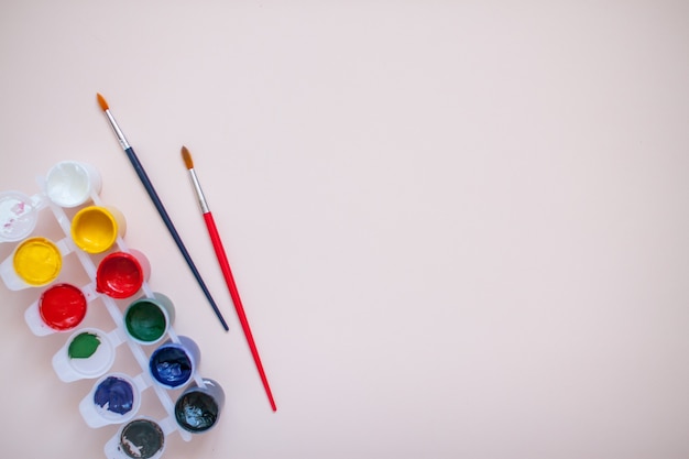 Bright paints and two brushes on a light pink background. Preparation for drawing