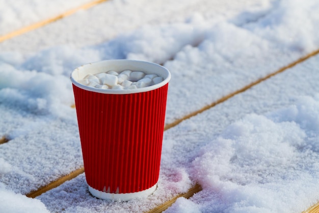 雪の上に温かい飲み物が入った明るい紙コップ