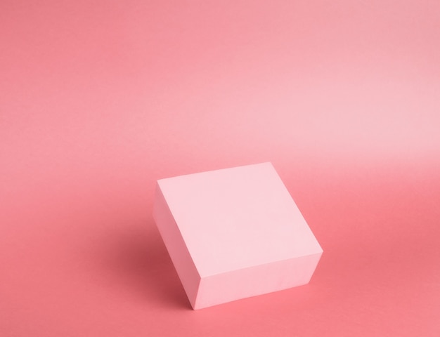 Piedistallo luminoso di un cubo su uno sfondo di carta in rosa