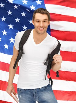Immagine luminosa di uno studente in viaggio con zaino e libro sopra la bandiera americana