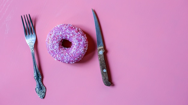 Bright pink donut in glaze with knife and fork