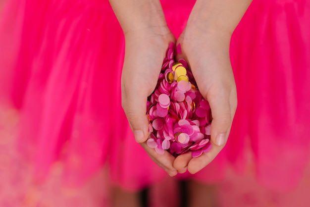 Bright pink and gold paper confetti in the palms of a birthday girl in a dress at a party