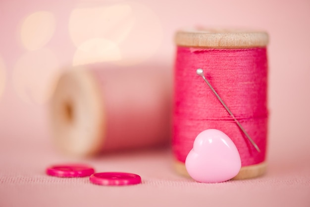 Photo bright pink thread roll with needle and heart shape button closeup. homemade sewing concept.