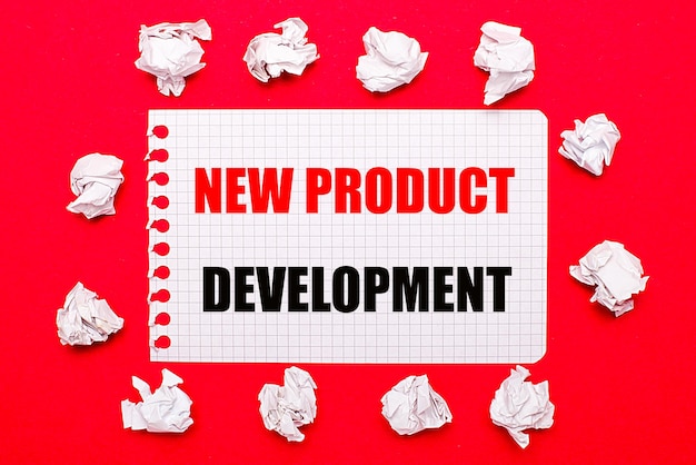 On a bright red background white crumpled sheets of paper and a sheet of paper with the text NEW PRODUCT DEVELOPMENT