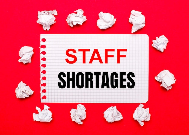 On a bright red background, white crumpled sheets of paper and a sheet of paper with the text STAFF SHORTAGES