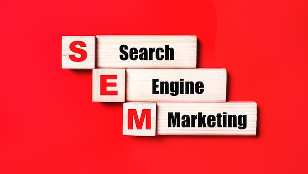 На ярко-красном фоне деревянные кубики и блоки с текстом SEM Search Engine Marketing Производство деревянных игрушек