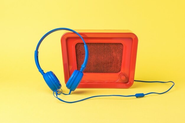 밝은 빨간색 복고풍 라디오 및 노란색 배경에 파란색 헤드폰. 사운드 및 비디오 재생 기술.