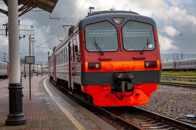 밝은 빨간색 기차가 도시 여객 운송의 기차역 플랫폼까지 끌어옵니다.