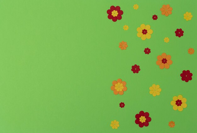 Bright red, yellow and orange paper flowers on green background with copy space