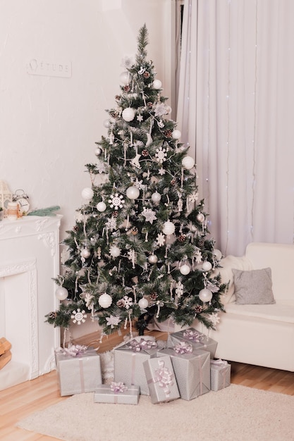 In a bright room with a white sofa there is a green Christmas tree decorated with white decor