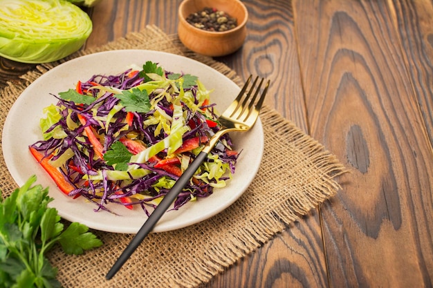 Bright salad of purple cabbage white cabbage bell pepper in a plate on a dark table Bright salad of fresh vegetables Food background Vegetarian dish View from above Copy space