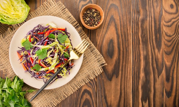 Яркий салат из фиолетовой капусты, белокочанной капусты, болгарского перца в тарелке на темном столе, яркий салат из свежих овощей, фон еды, вегетарианское блюдо, вид сверху, копия пространства