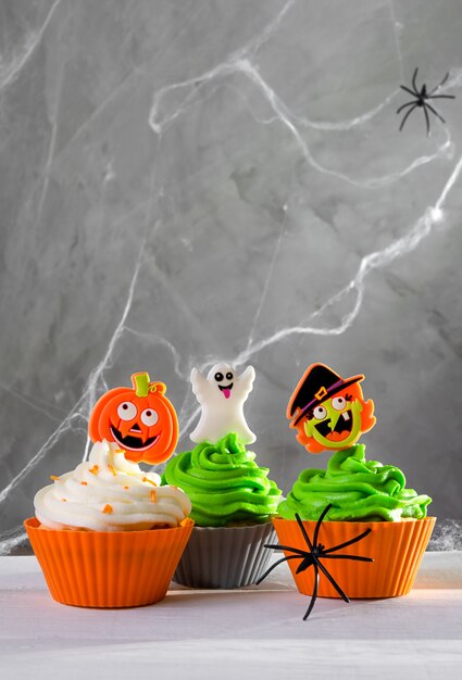 Яркие страшные кексы на хэллоуин на темном фоне с паутиной. цветные кремы и декор.