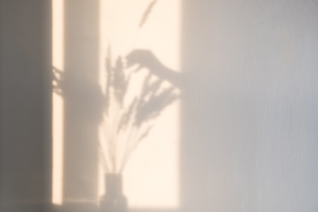 A bright shadow of a woman's hand adds a spike of dry grass to a bouquet of dried flowers against a light wall